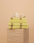 Stack of Citrus Yellow striped Kobn Bathroom towels, hand towel and bathmat, folded on a plinth with a clam on top.