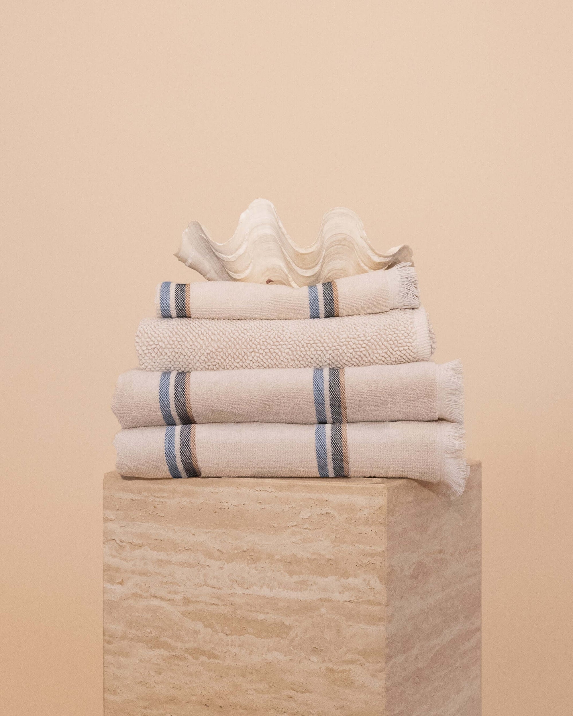 Stack of Kobn towels, bathmat and hand towel in Ecru featuring blue and tan stripes.