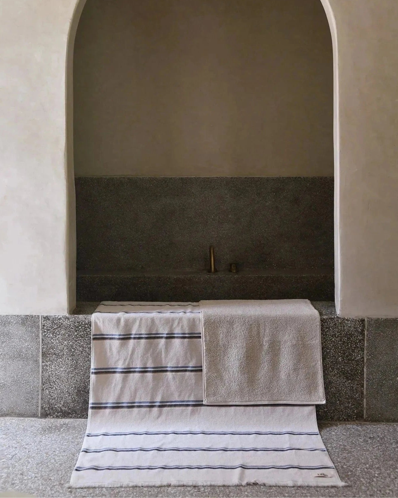 A bathroom with an arch entrance to the bath with a striped towel and bath mat draped over the bath.