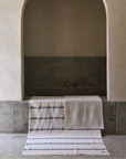 A bathroom with an arch entrance to the bath with a striped towel and bath mat draped over the bath.