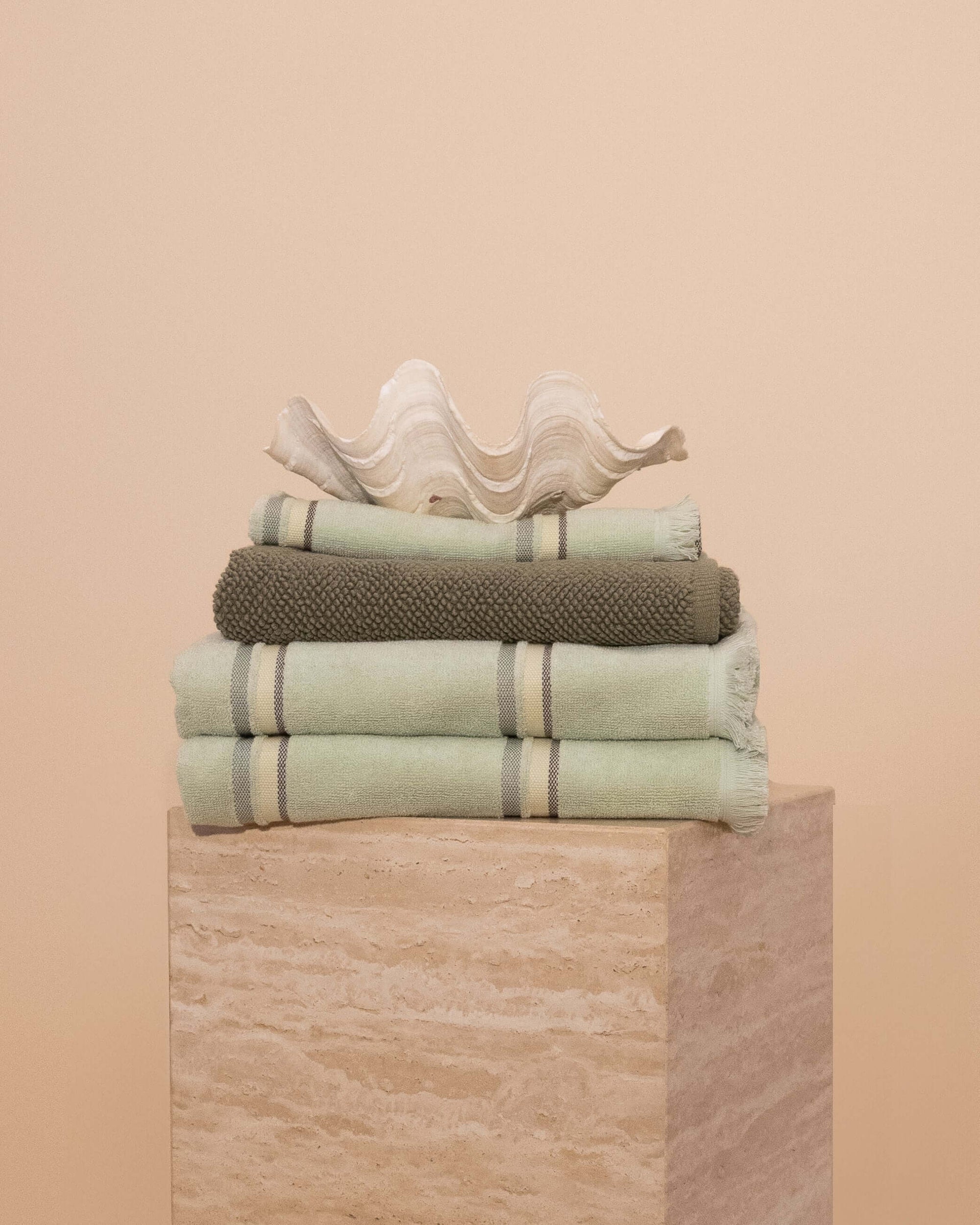 Matcha bathroom set folded on a travertine plinth with a clam shell on top.