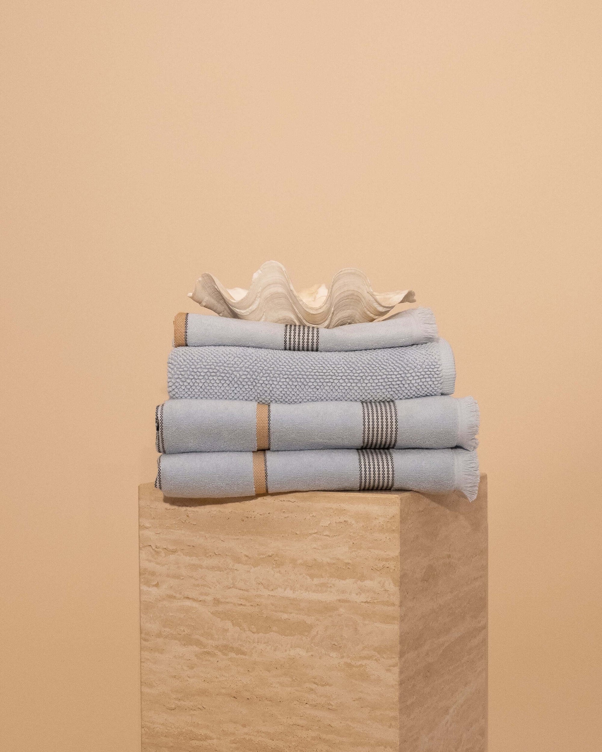 Stack of Mist Bathroom towels , hand towel and bathmat folded on a travertine plinth.
