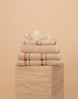Folded Kobn Sand towels, bathmat and hand towel on a travertine plinth featuring the stripe and fringe details.