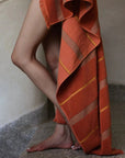 A womans legs with a towel in Tamarillo with stripes is draped to the side of them.