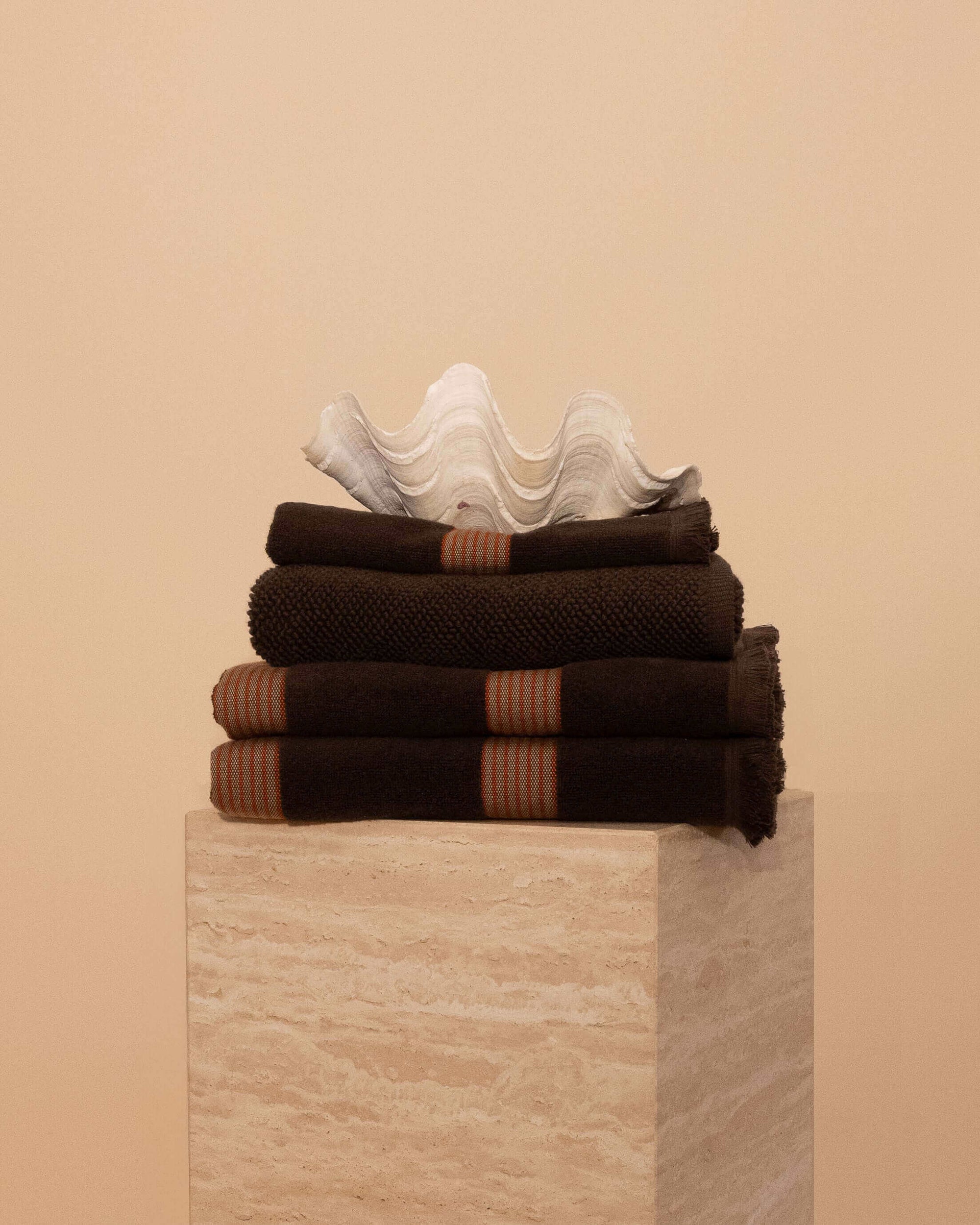 Kobn Bathroom Set in Umber with contrast stripes stacked on a travertine plinth. Set includes 2 towels, 1 bath mat, 1 hand towel.
