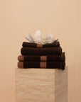 Kobn Bathroom Set in Umber with contrast stripes stacked on a travertine plinth. Set includes 2 towels, 1 bath mat, 1 hand towel.