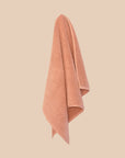 Textured chunky weave bathmat in a neutral clay colour hanging on a butter yellow background.