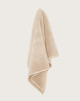 Chunky cotton textured bathmat in sand colour hanging against a neutral wall.