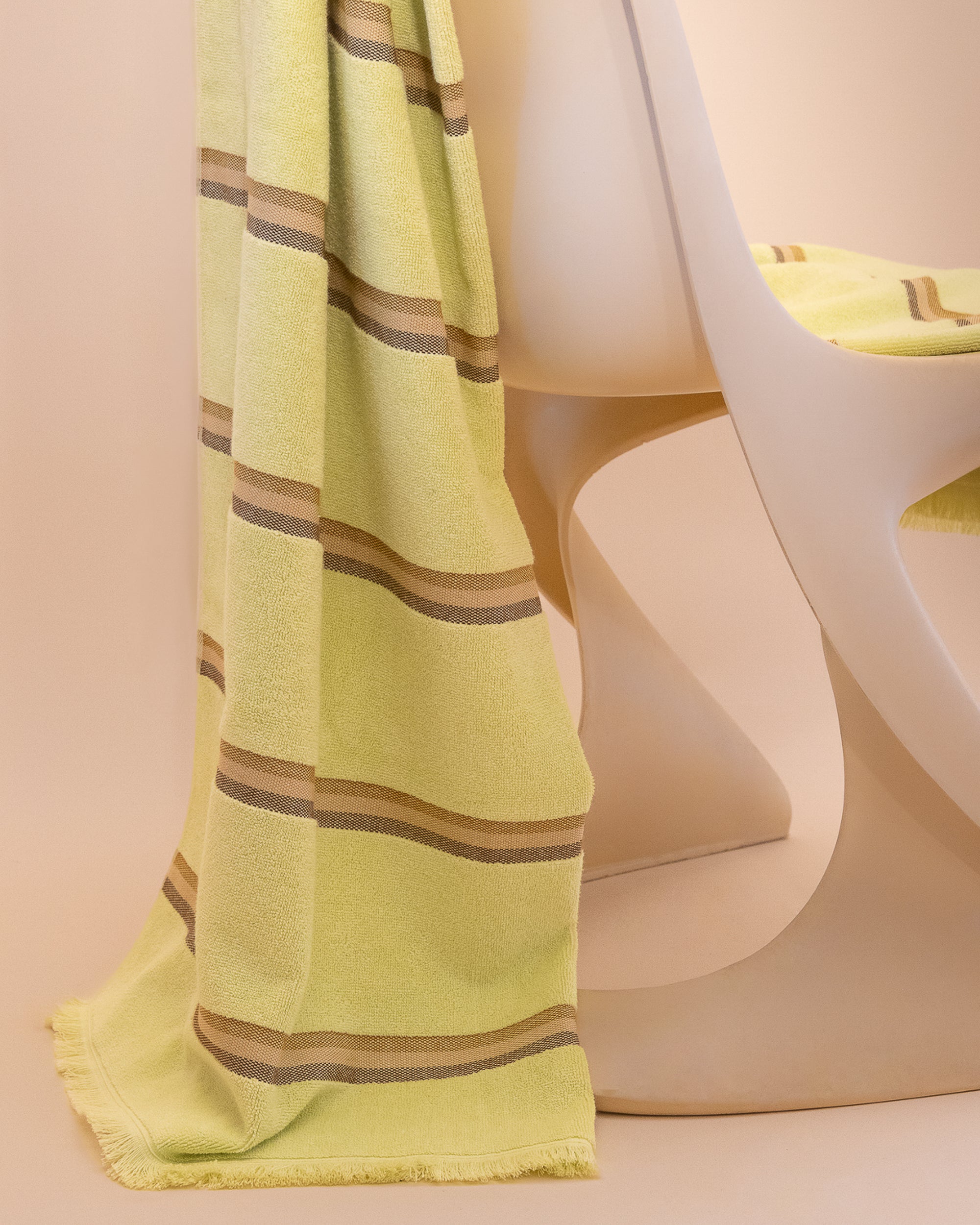 Citrus towel by Kobn with brown stripes draped over a chair on a beige background