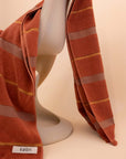 Striped Tamarillo towel by Købn draped over a chair on a beige background .