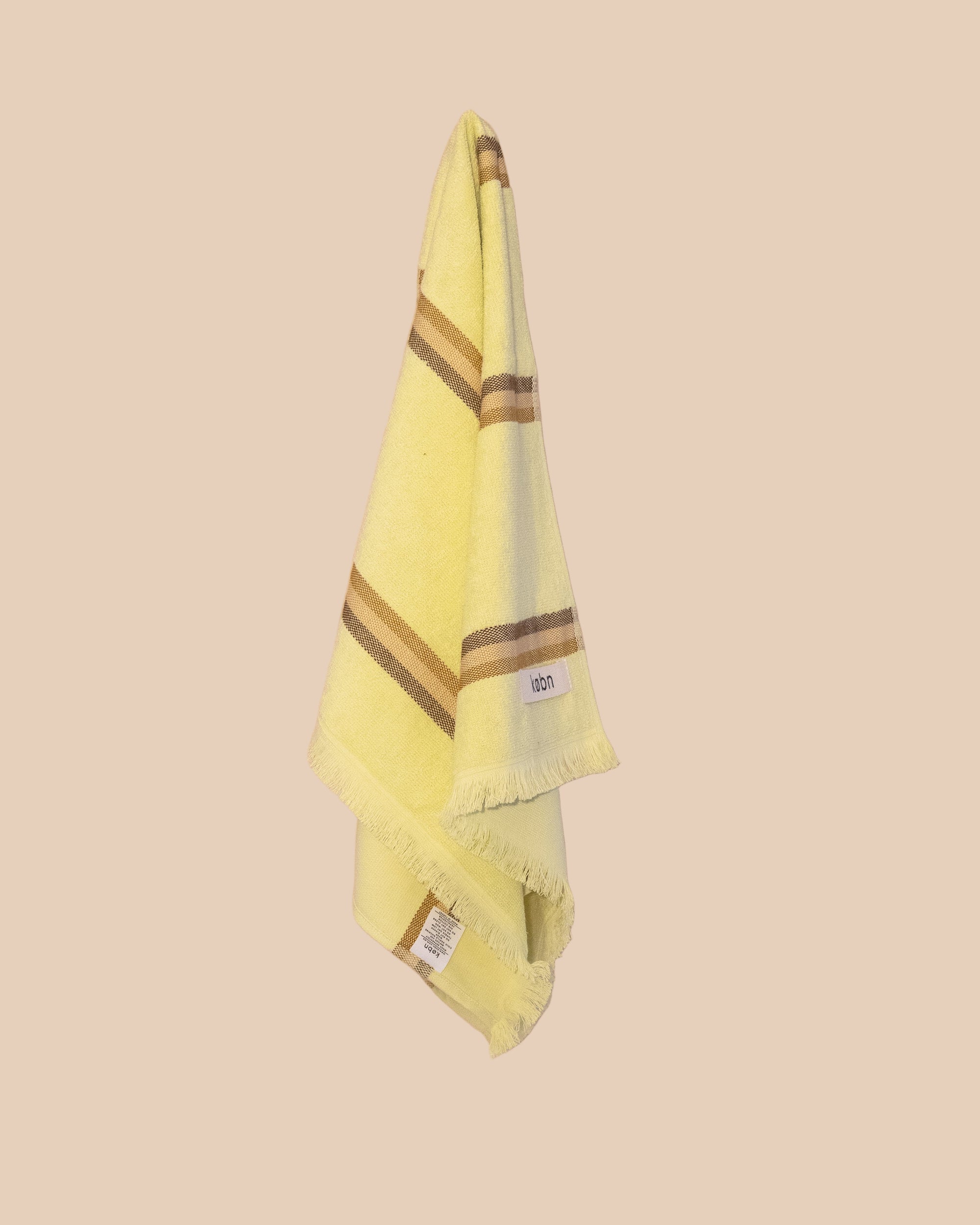 Bright yellow hand towel with brown stripes hanging on a netural wall.