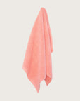 Pink bathmat with a chunky cotton weave hanging on a butter yellow background.