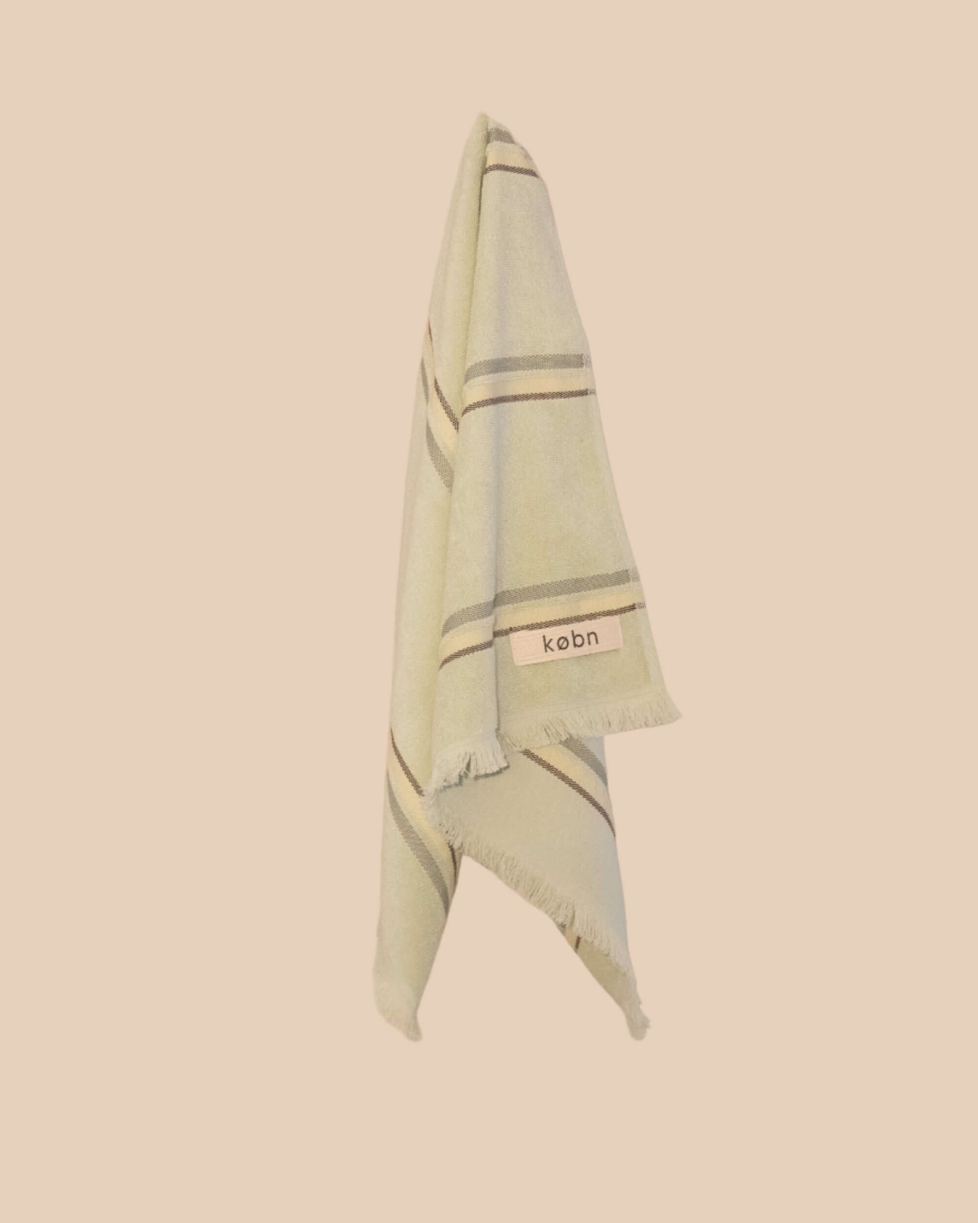 Light green hand towel with striped pattern and 'kebn' label on a beige background