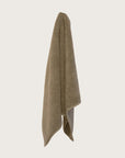 Olive coloured chunky weave cotton bahtmat hanging on a neutral background.