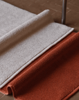 Two bathmats in Ecru and Tamarillo on floor with chunky cotton texture.