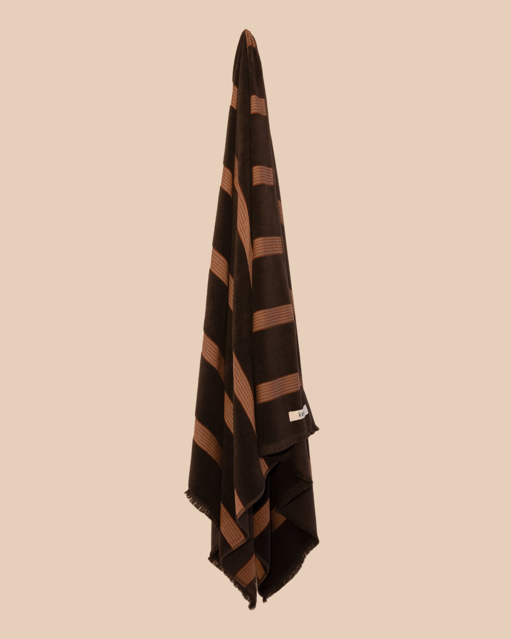 Chocolate brown bath towel with red stripes and fringing hanging on a butter yellow background.