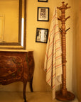 Wooden coat stand with a striped towel against a beige wall with framed pictures.