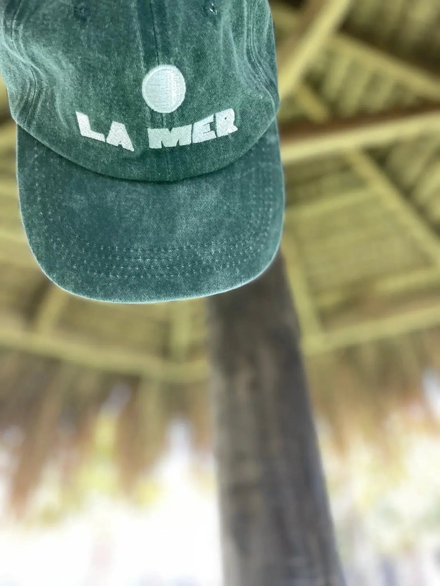 Stonewashed green La Mer emboidered cap hanging under an umbrella.
