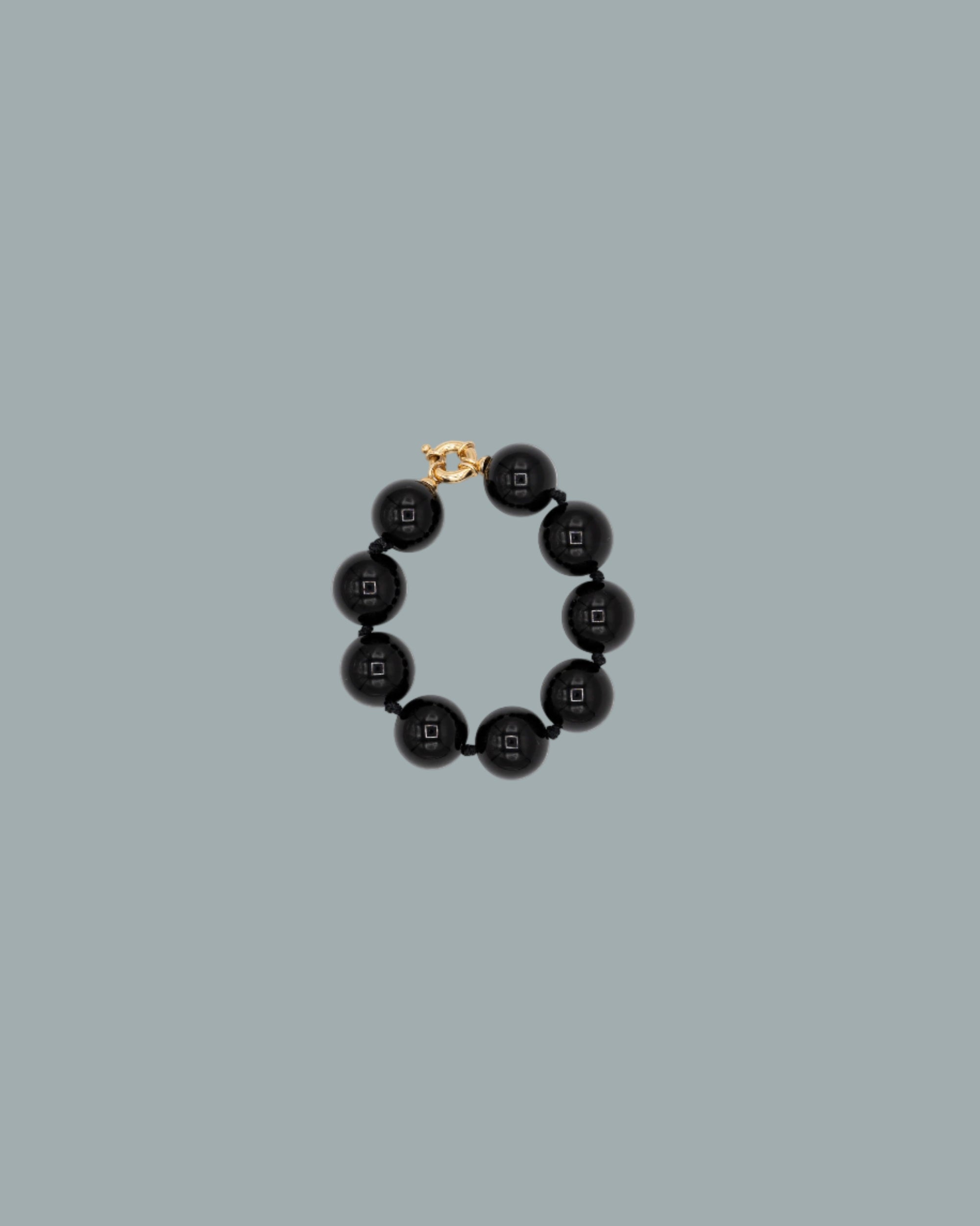 Black beaded bracelet with gold clasp on a blue background