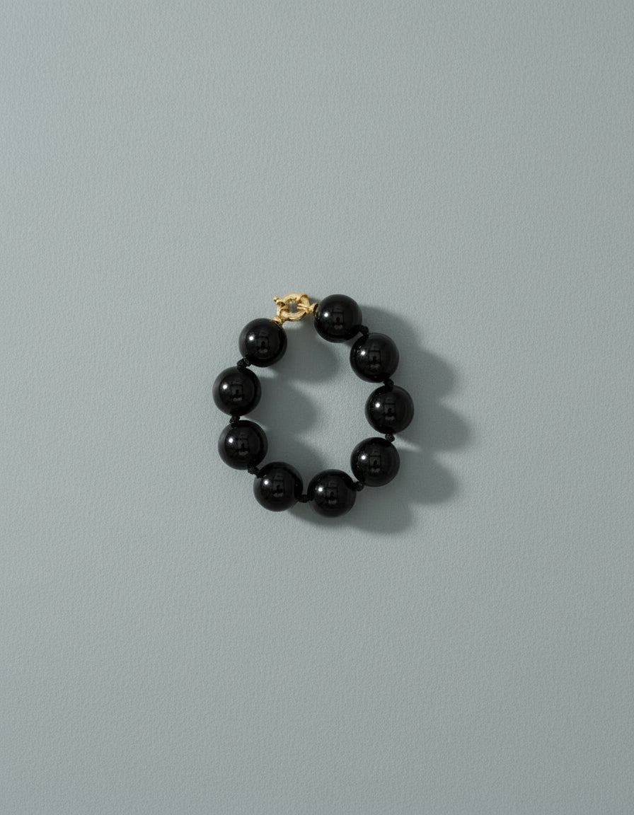 Black beaded bracelet with gold clasp on a blue background
