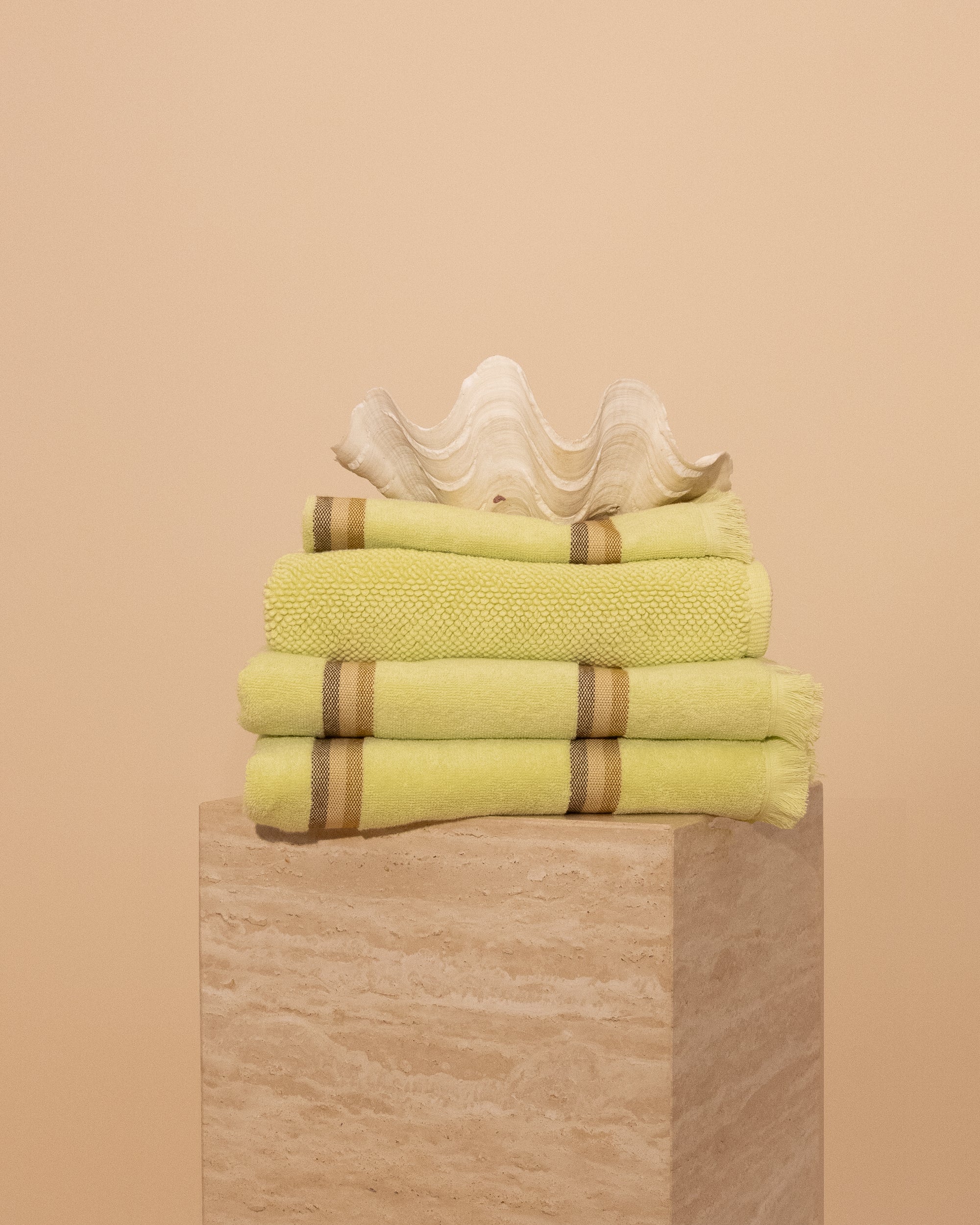 Stack of Citrus Yellow striped Kobn Bathroom towels, hand towel and bathmat, folded on a plinth with a clam on top.
