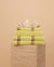 Stack of Citrus Yellow striped Kobn Bathroom towels, hand towel and bathmat, folded on a plinth with a clam on top.
