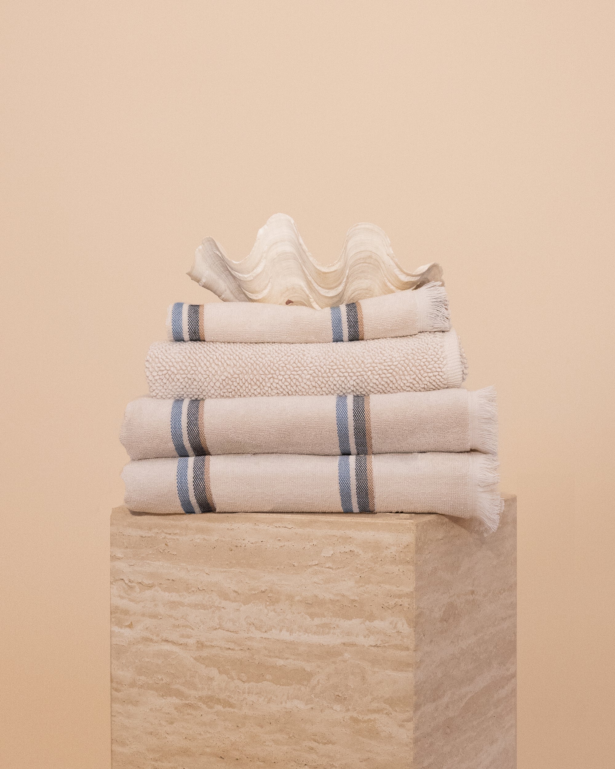 Stack of Kobn towels, bathmat and hand towel in Ecru featuring blue and tan stripes. 