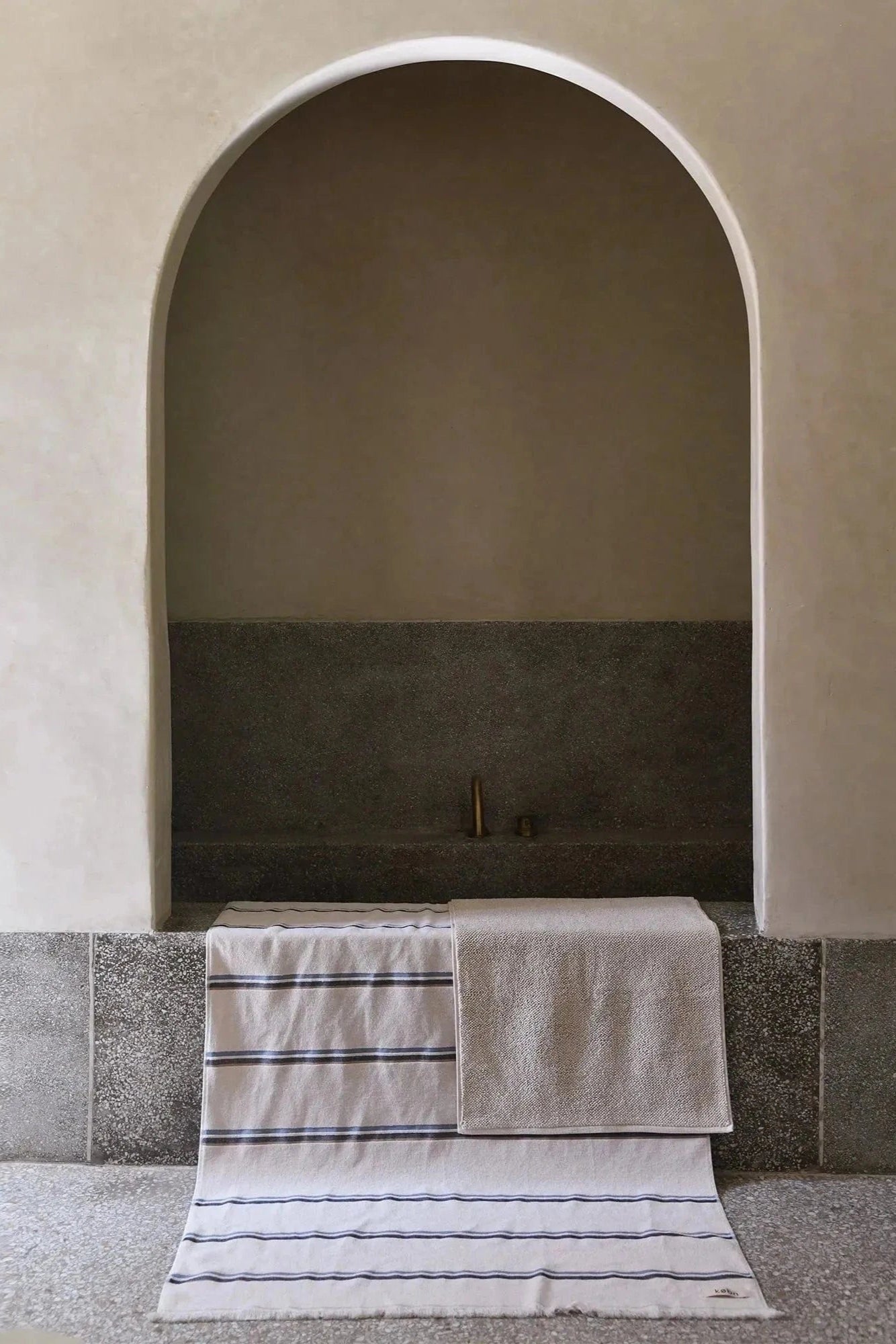A bathroom with an arch entrance to the bath with a striped towel and bath mat draped over the bath. 