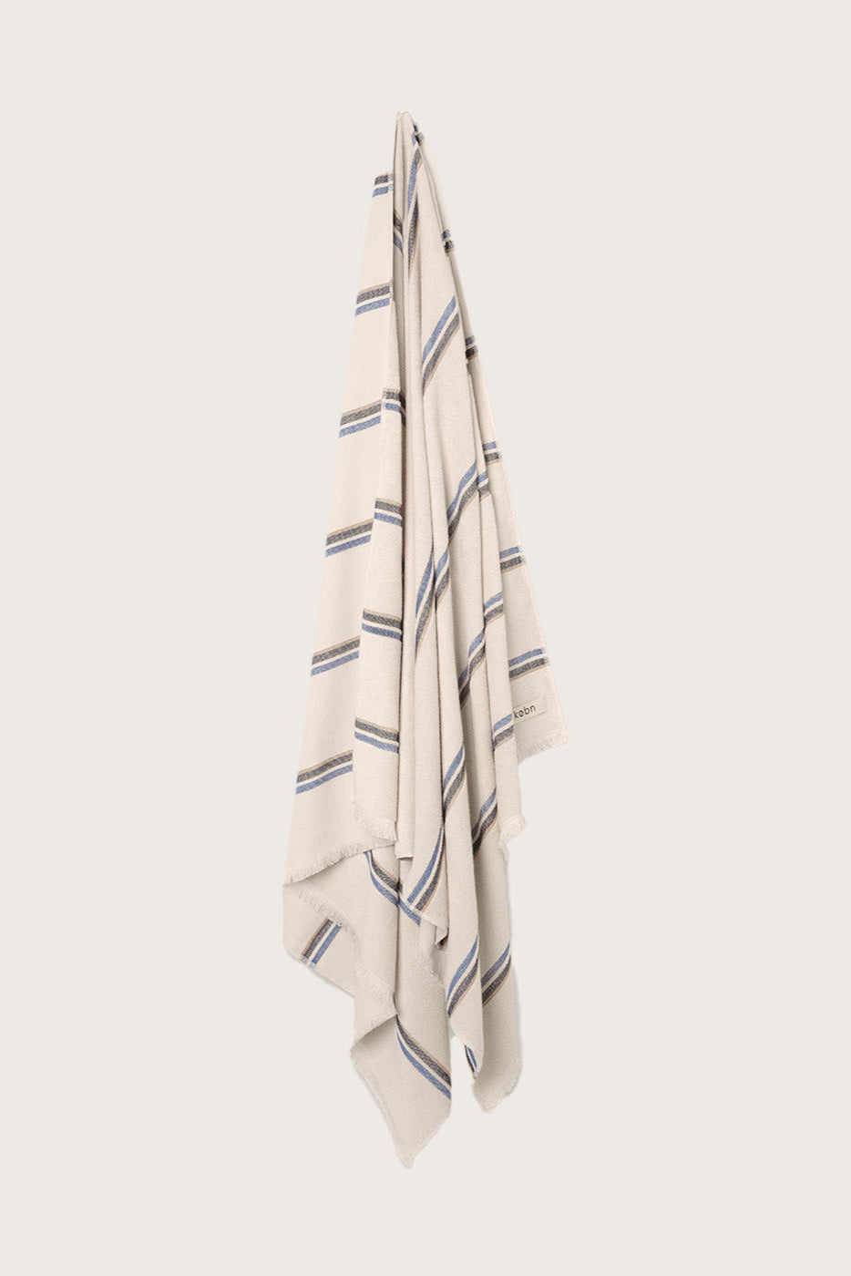 Købn Ecru Towel with stripes and raw edge fringing hanging on a hook