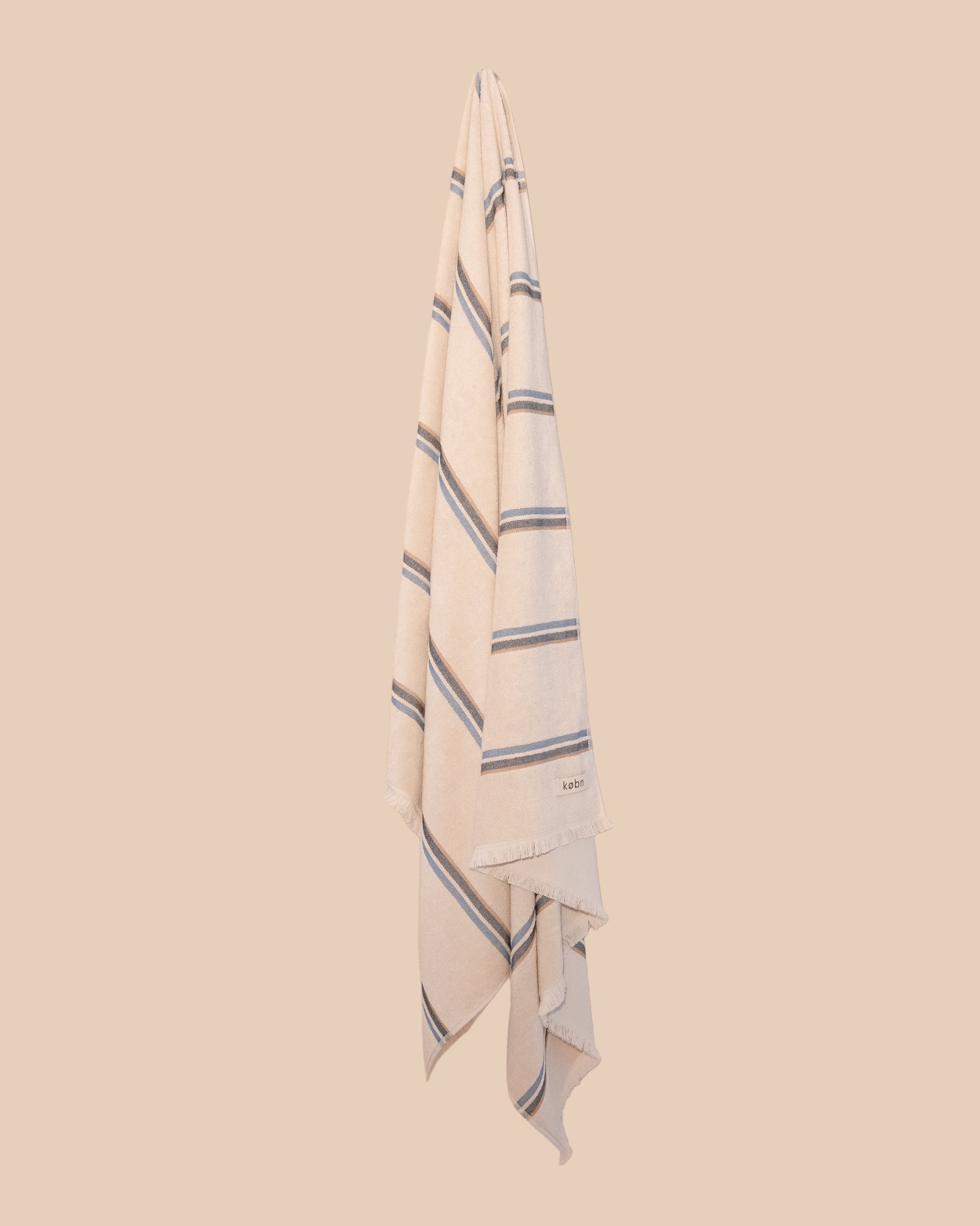 Striped kobn towel in ecru colour with blue stripes hanging on a beige background