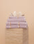 Folded stack of Lilac Kobn towels, hand towel and bathmat on a travertine plinth and topped with a clam shell. 