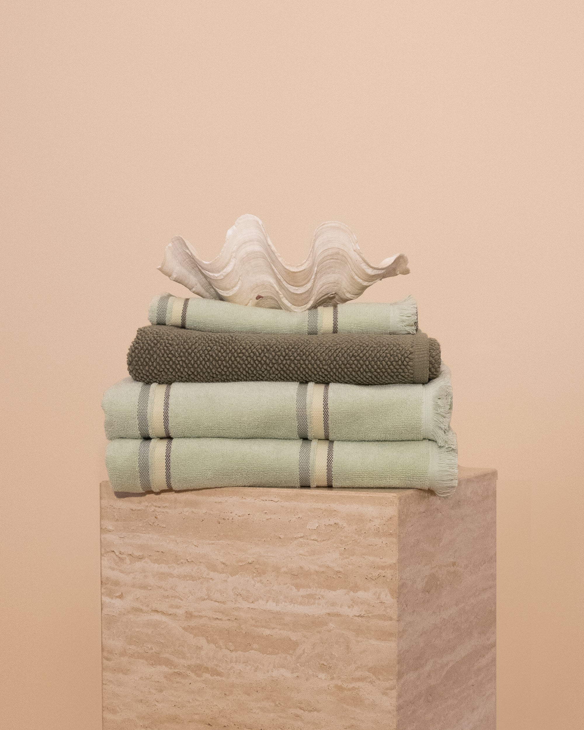 Matcha bathroom set folded on a travertine plinth with a clam shell on top.