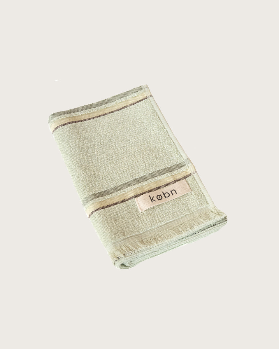 Folded mint hand  towel with stripes and 'kobn' branding on a light beige background