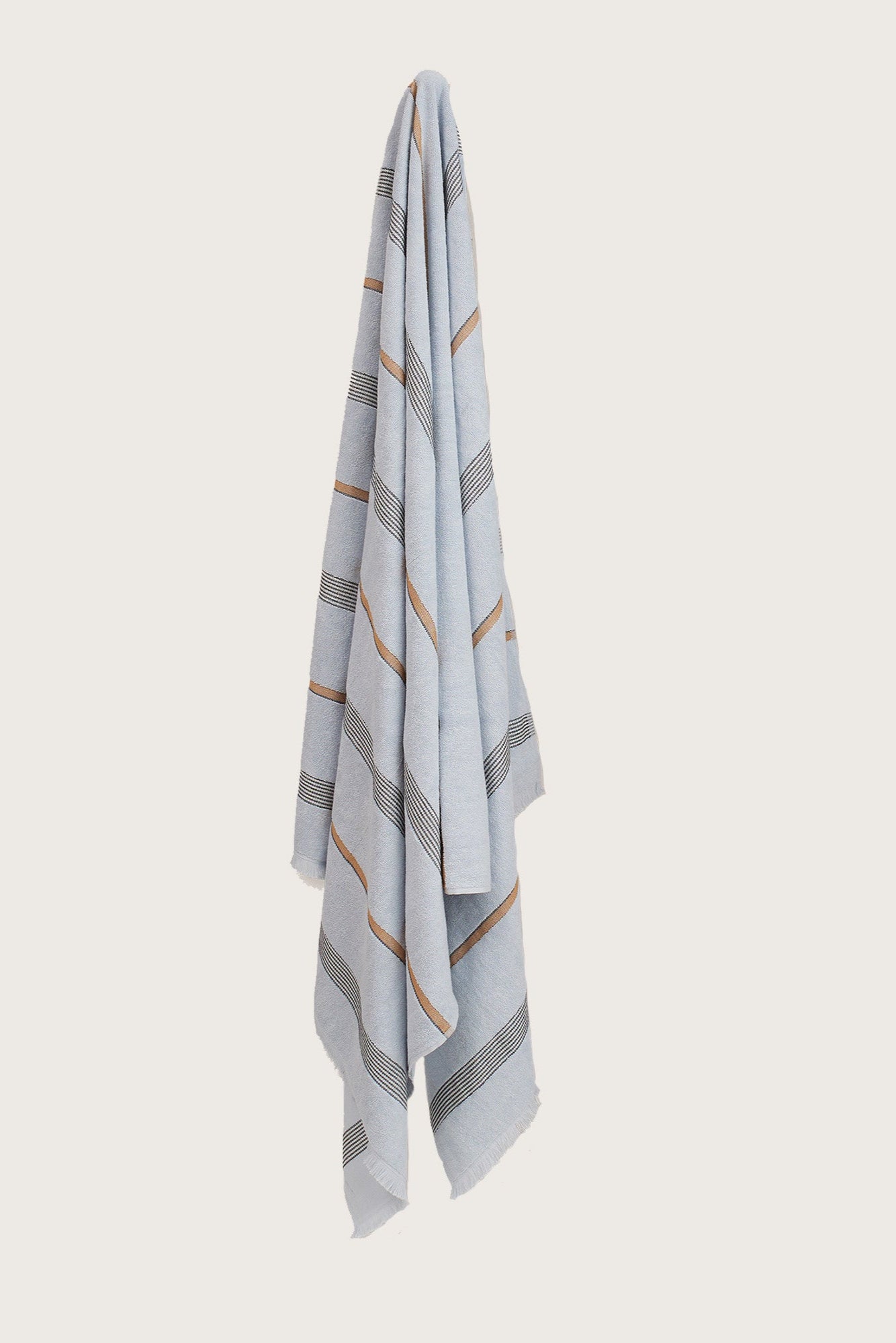 Købn Mist Towel with stripes and raw edge fringing hanging on a hook