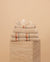 Folded Kobn Sand towels, bathmat and hand towel on a travertine plinth featuring the stripe and fringe details. 