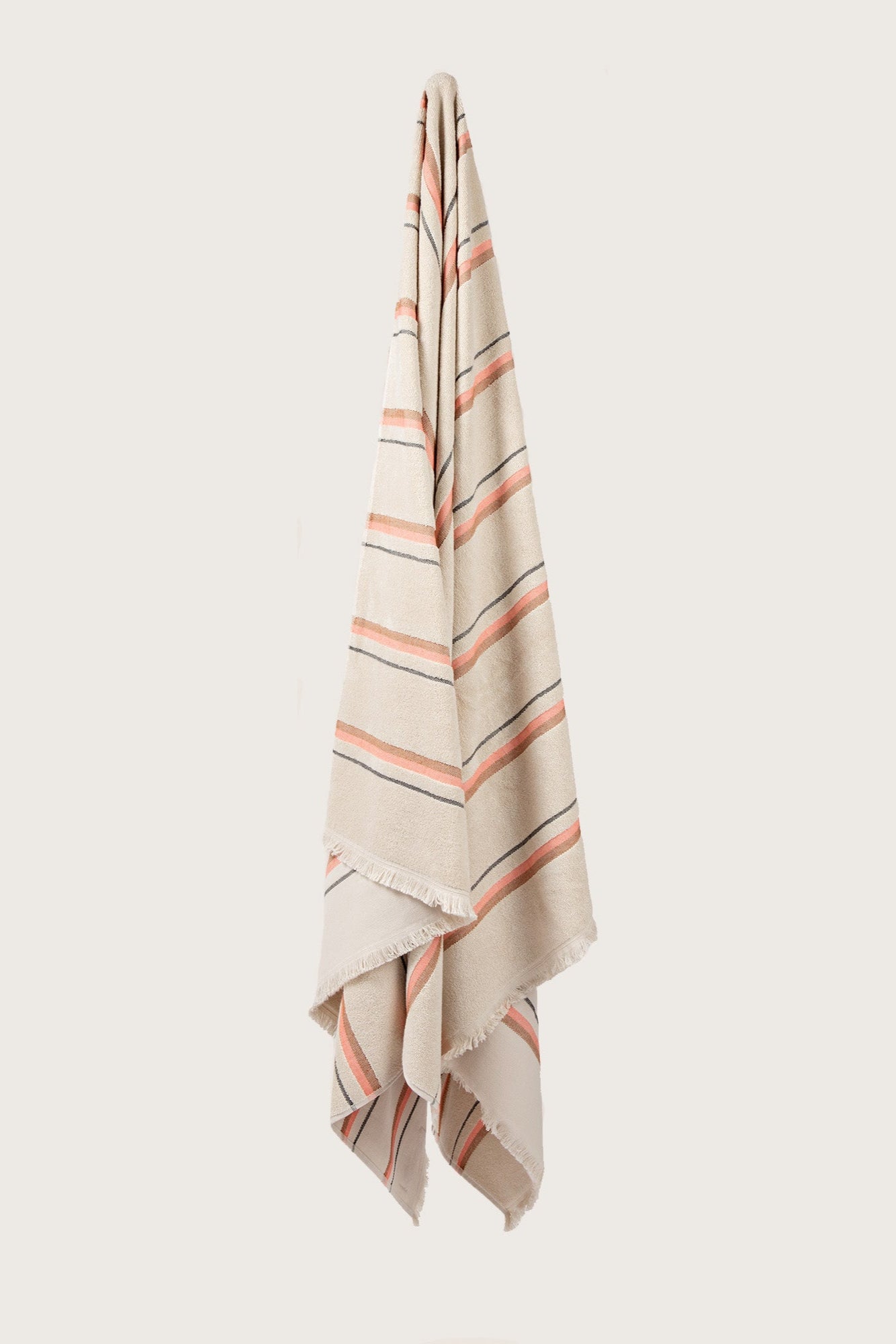 Købn Sand Towel with stripes and raw edge fringing hanging on a hook