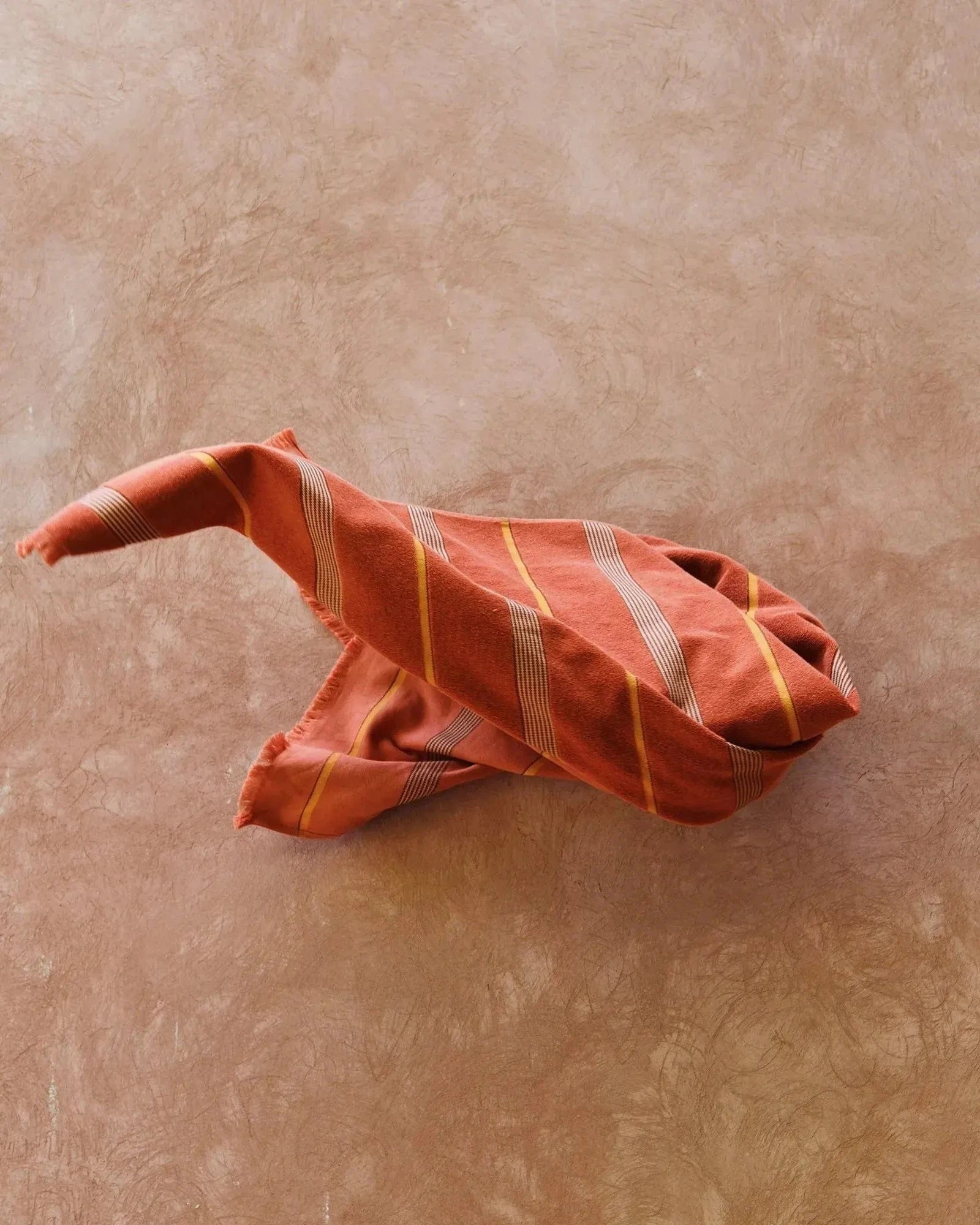 A Tamarillo Hand Towel falling against a blush pink rendered wall. 