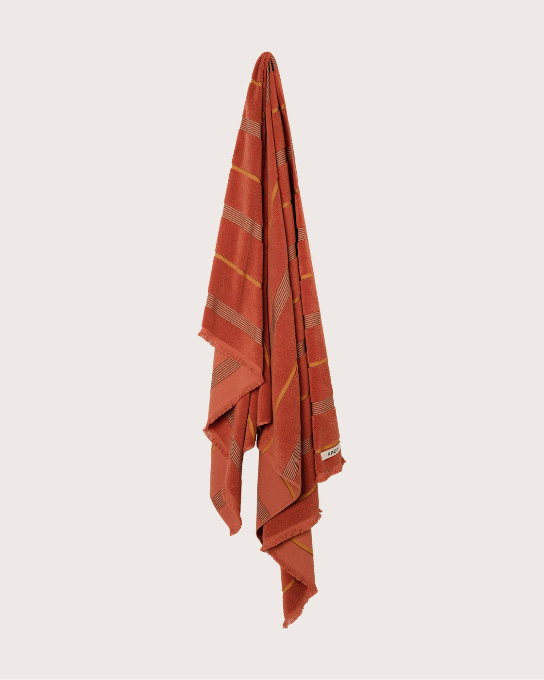 Købn Tamarillo Towel with stripes and raw edge fringing hanging on a hook