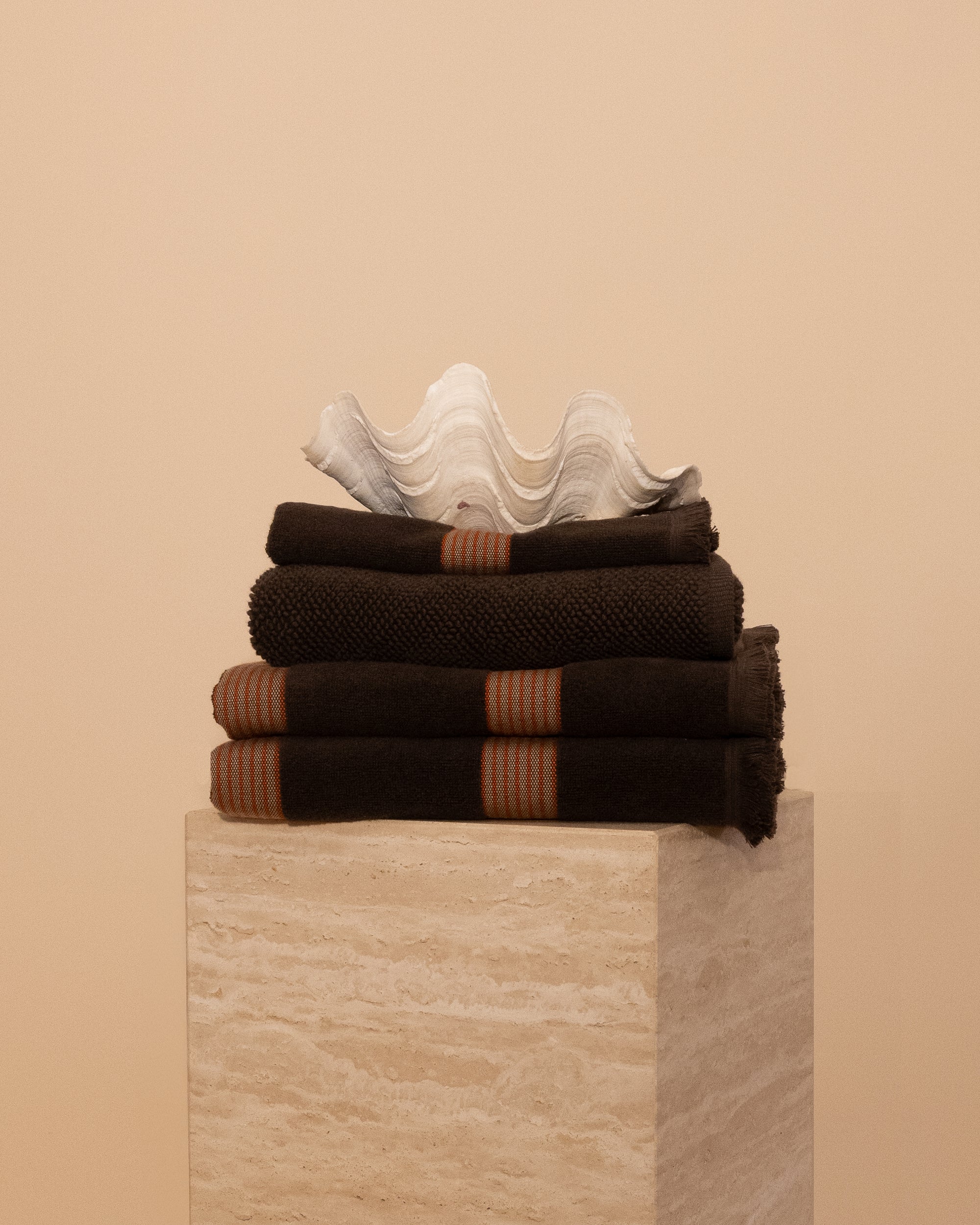 Kobn Bathroom Set in Umber with contrast stripes stacked on a travertine plinth. Set includes 2 towels, 1 bath mat, 1 hand towel. 