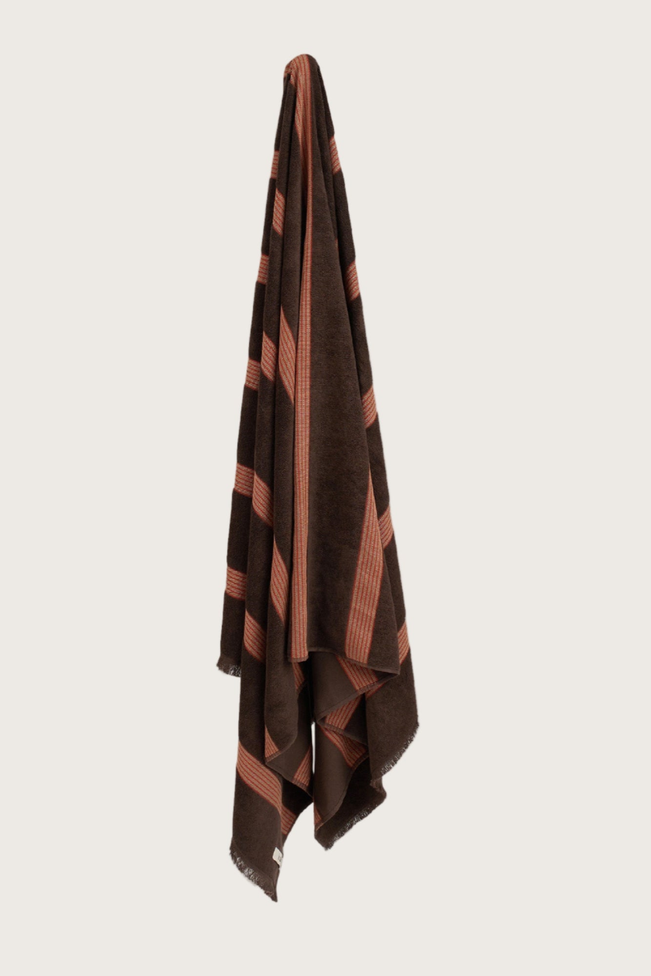 Købn Umber Towel with stripes and raw edge fringing hanging on a hook