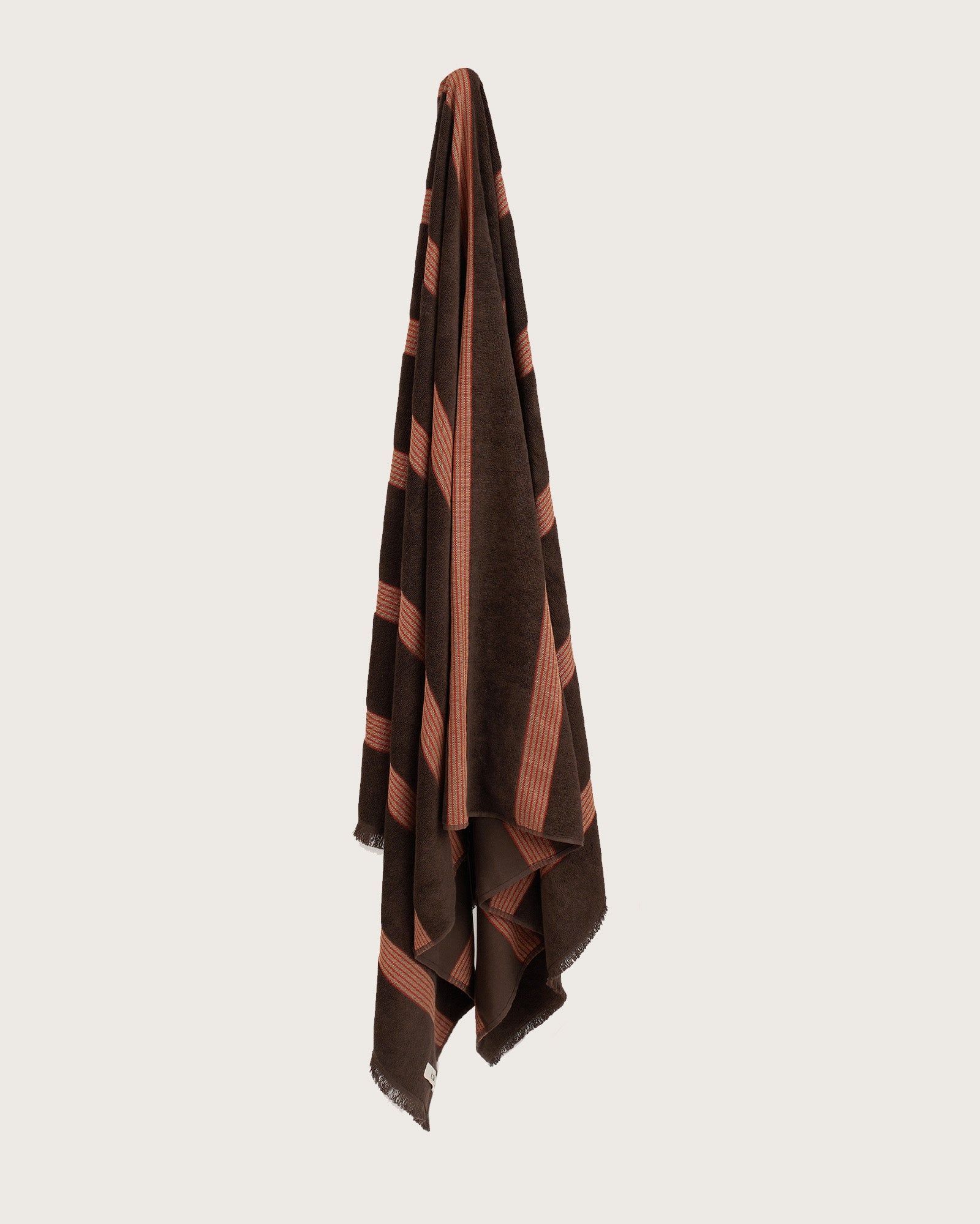 Købn Umber Towel with stripes and raw edge fringing hanging on a hook