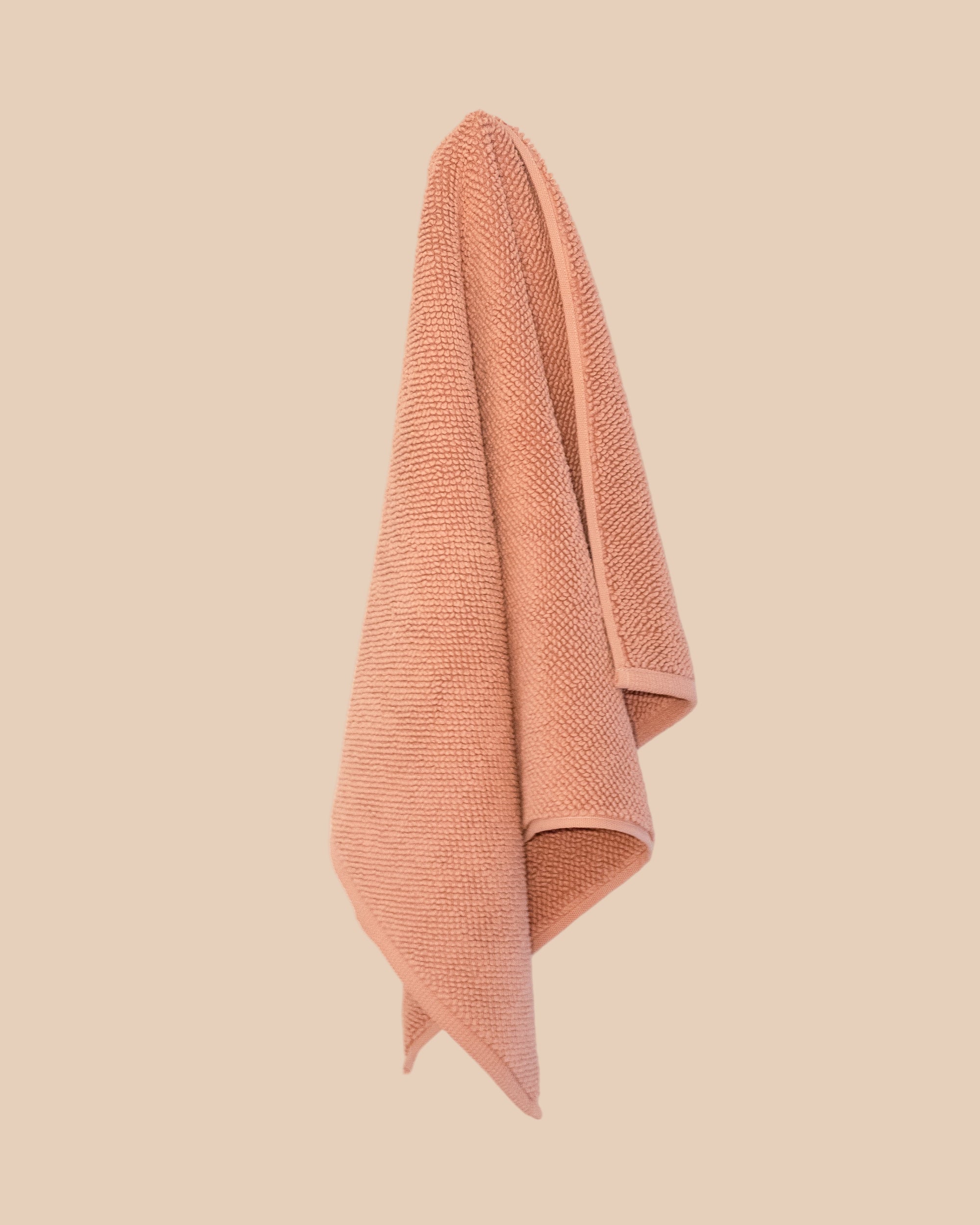 Textured chunky weave bathmat in a neutral clay colour hanging on a butter yellow background.