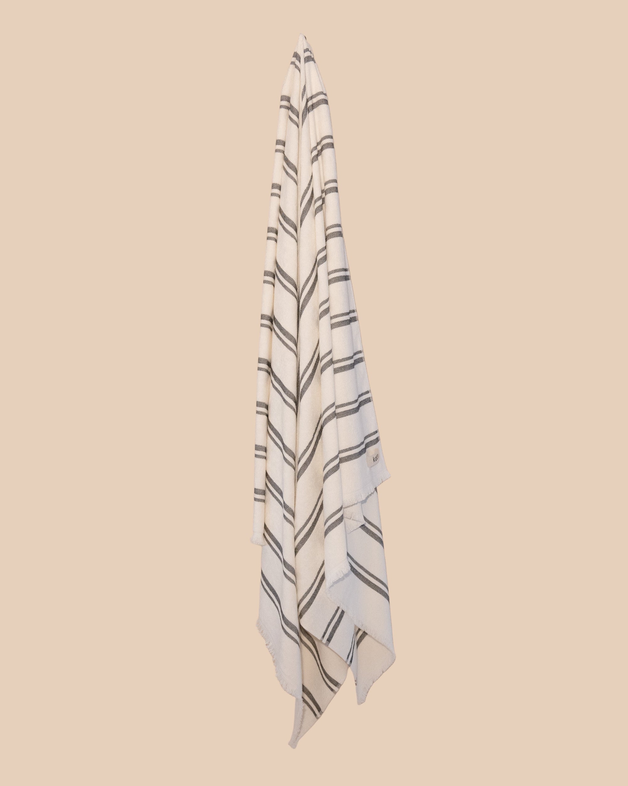 Kobn Crema towel with black stripes hanging on a butter yellow background