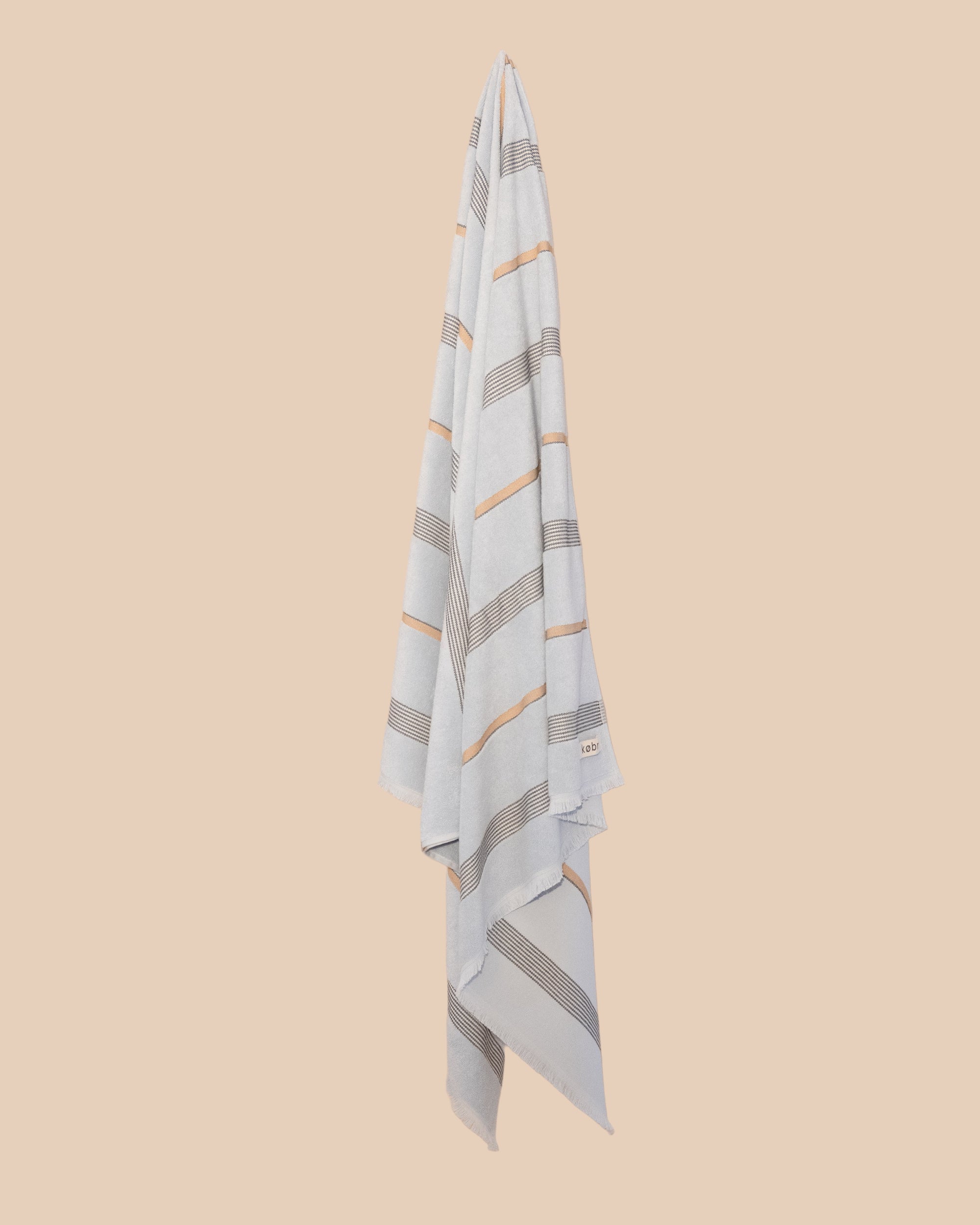 Pale Blue Beach Towel with stripes hanging on a butter yellow background