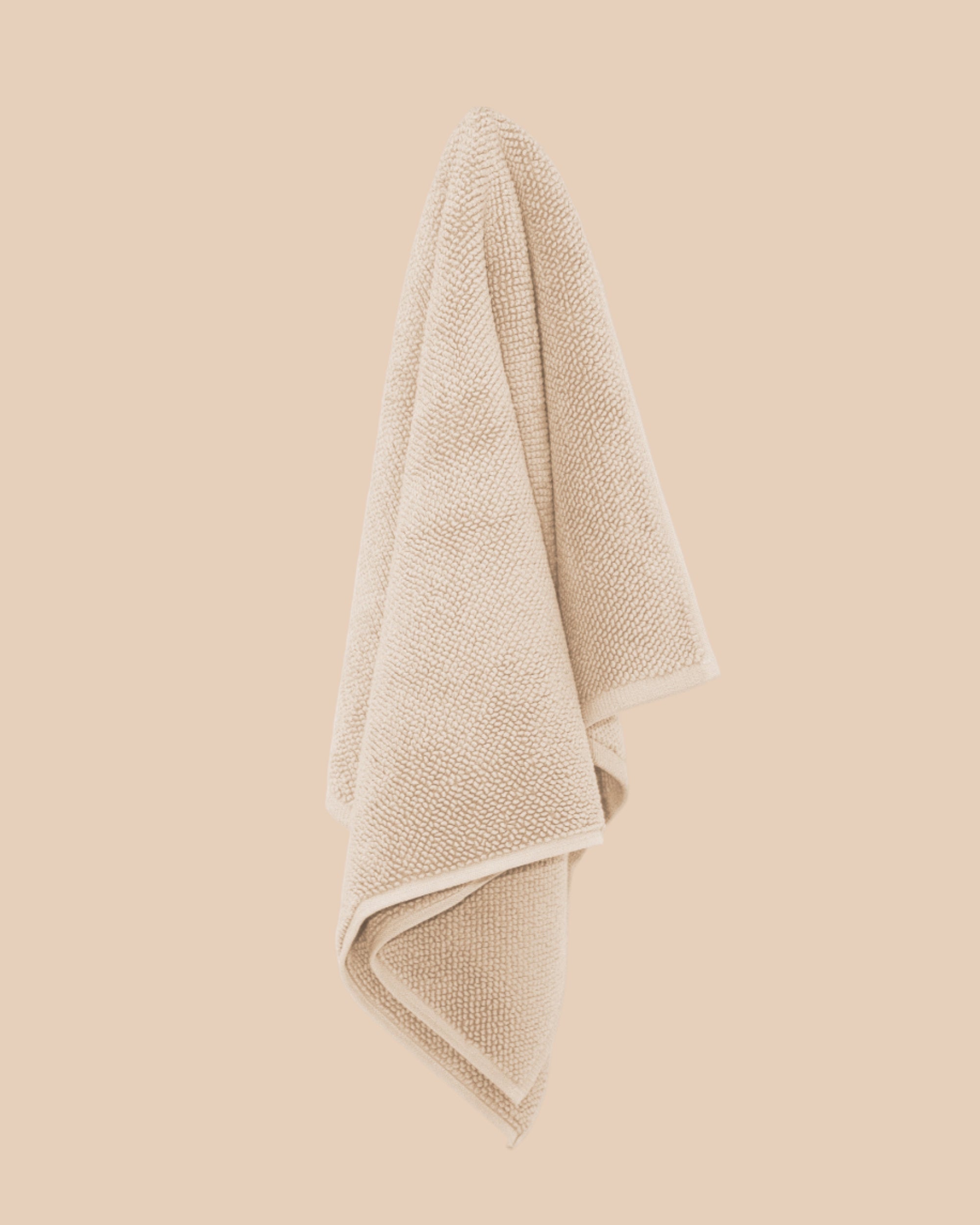 Chunky cotton textured bathmat in sand colour hanging against a neutral wall. 