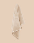 Chunky cotton textured bathmat in sand colour hanging against a neutral wall. 
