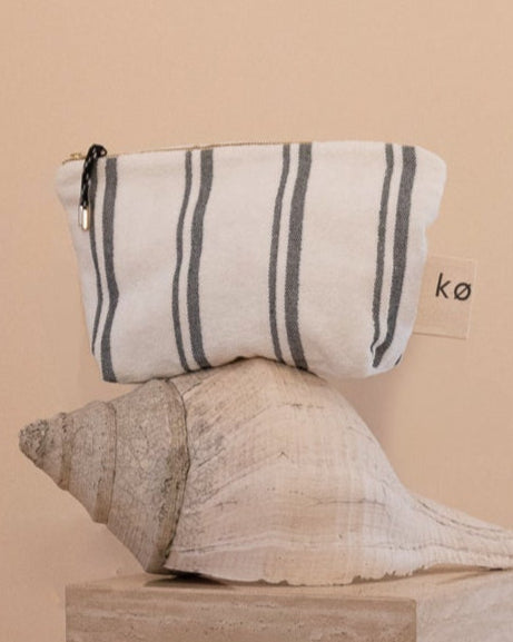 Kobn towelling Crema pouch perched on a large conch shell with a brand label, gold zip and tassle. For use as a clutch or organiser. 