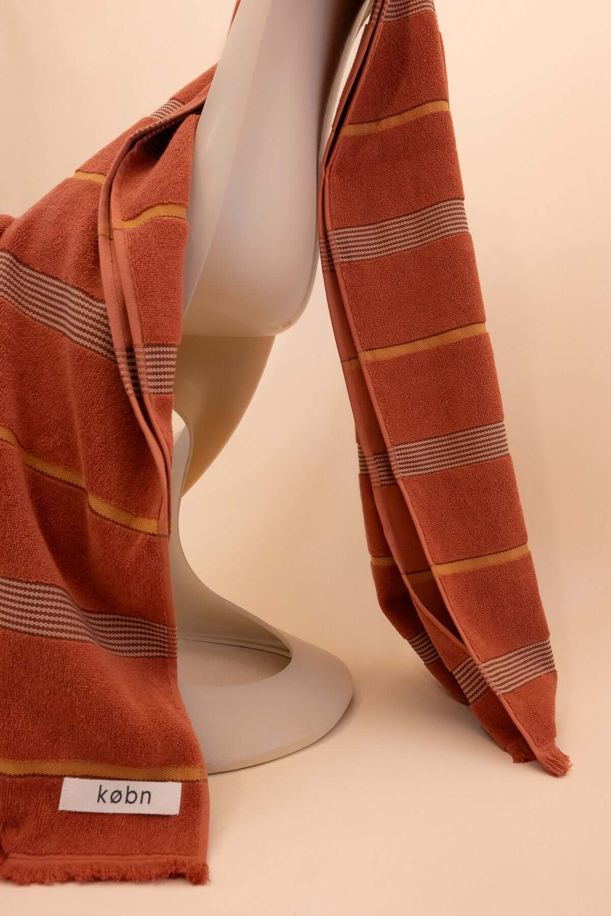 Striped Tamarillo  towel by Købn draped over a chair on a beige background .