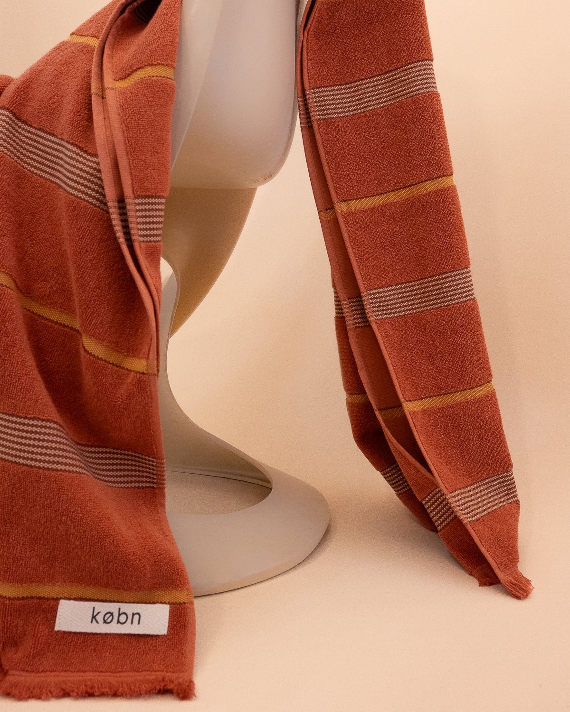 Striped Tamarillo  towel by Købn draped over a chair on a beige background .