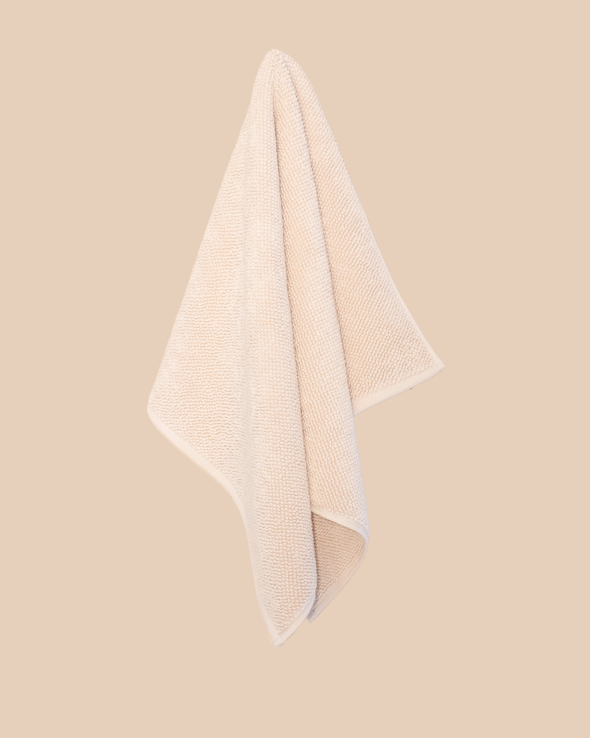 Chunky cotton weave bathmat in ecru colour hanging on a soft beige background. 